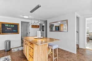 A modern kitchen with a wooden island, pendant lights, and a welcome sign. - Warm & Welcoming 5BR Home (South Burlington)