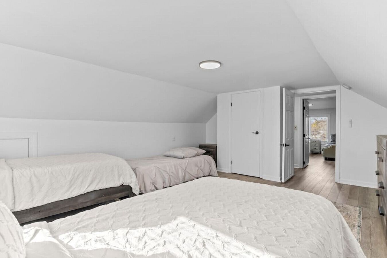 Une chambre avec deux lits, une armoire et une porte donnant sur une autre pièce.
