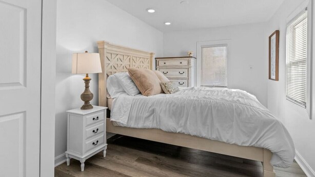 A bedroom with a bed, bedside table, lamp, and a dresser.