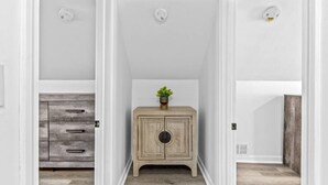 A narrow hallway with a wooden cabinet and a plant on top, leading to a room with a white door.