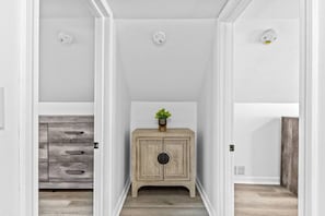 A narrow hallway with a wooden cabinet and a plant on top, leading to a room with a white door. - Warm & Welcoming 5BR Home (South Burlington)
