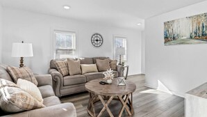 A living room with a sofa, armchair, round coffee table, and a painting on the wall.