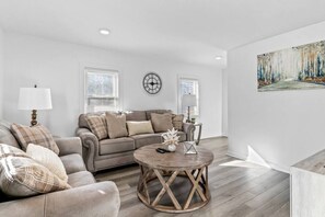 A modern living room with a sofa, a coffee table, and a painting on the wall. - Warm & Welcoming 5BR Home (South Burlington)