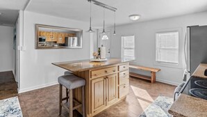A modern kitchen with a central island, wooden cabinets, pendant lighting, and a large refrigerator.
