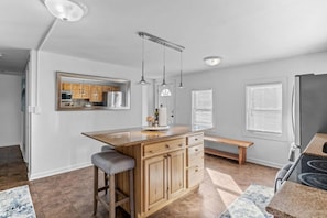 A modern kitchen with a central island, wooden cabinets, pendant lighting, and a large refrigerator. - Warm & Welcoming 5BR Home (South Burlington)