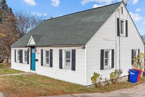 A white single-story building with a dark roof, a blue door, and black shutters on the windows. - Warm & Welcoming 5BR Home (South Burlington)