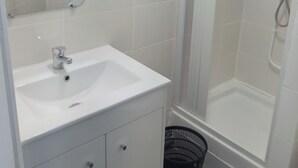 A bathroom with a white sink, mirror, and shower. - Hôtel Le Celtic (Montlucon)