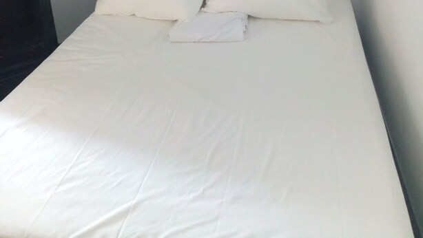 A neatly made bed with white bedding and pillows, a wall-mounted artwork depicting a path of stones, and a plain white wall. - Hôtel Le Celtic (Montlucon)