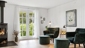 Una sala de estar con chimenea, dos sillones verdes, un otoman redondos y un cuadro en la pared.