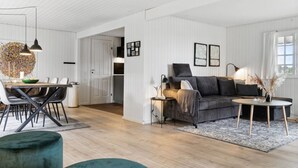 Una sala moderna con un sofá gris oscuro, una mesa de centro redonda y un comedor con una mesa y sillas de madera.