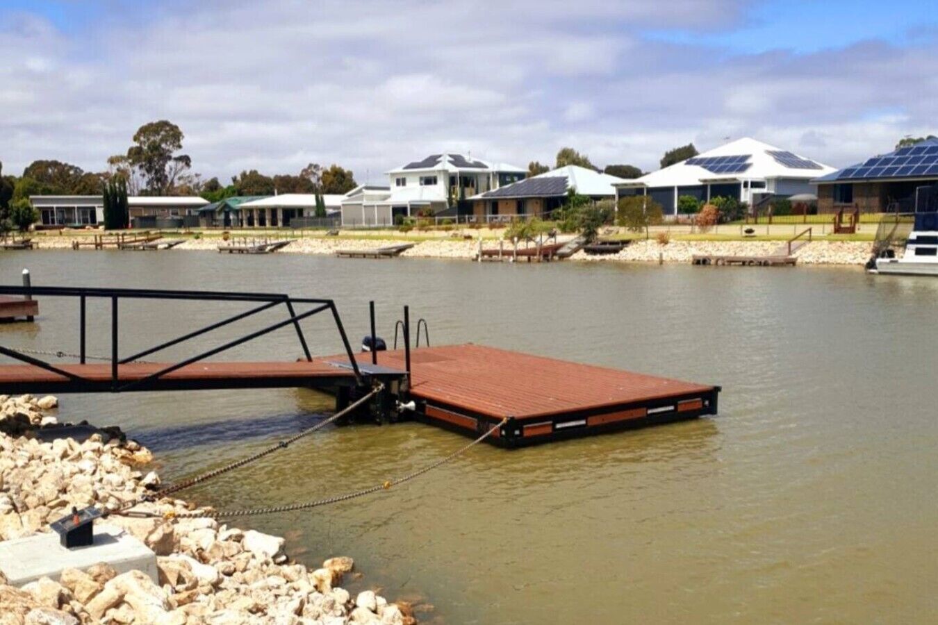 A waterfront property with a dock, houses with solar panels, and a calm river.