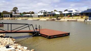 A waterfront property with a dock, houses with solar panels, and a calm river.