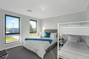 A modern hotel room with a large bed, bunk beds, and large windows offering a view of the outside.