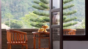 Een houten stoel en tafel met een decoratieve schaal op een balkon met uitzicht op een bebost gebied.