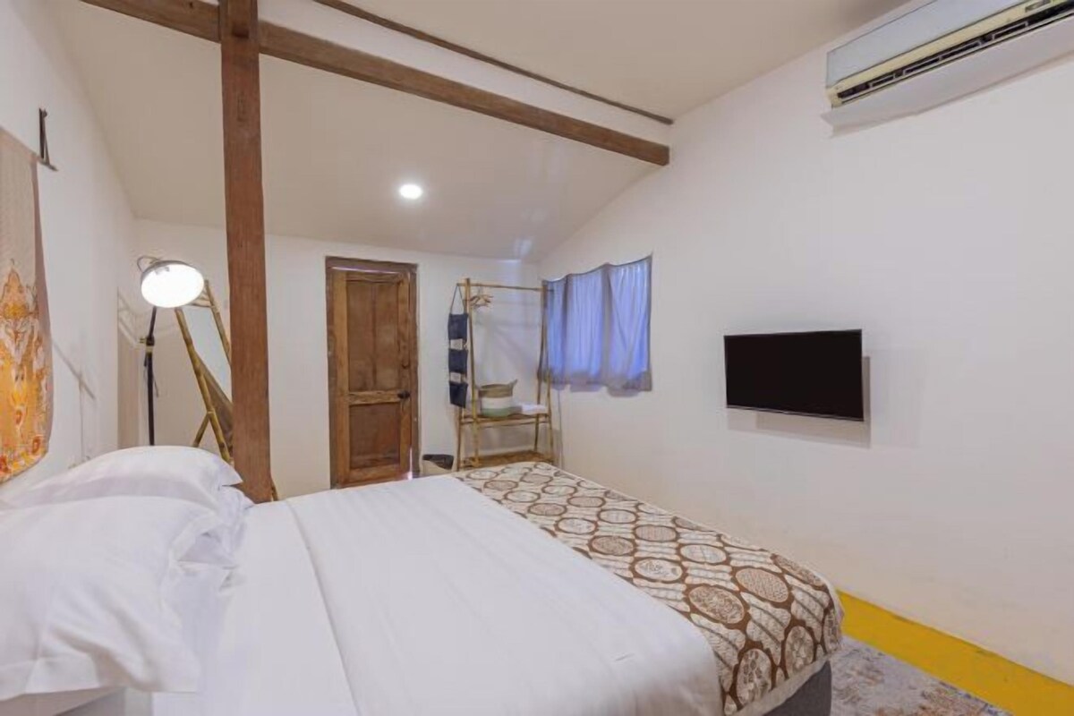 Un dormitorio con cama, escritorio, silla, lámpara, televisor y aire acondicionado.