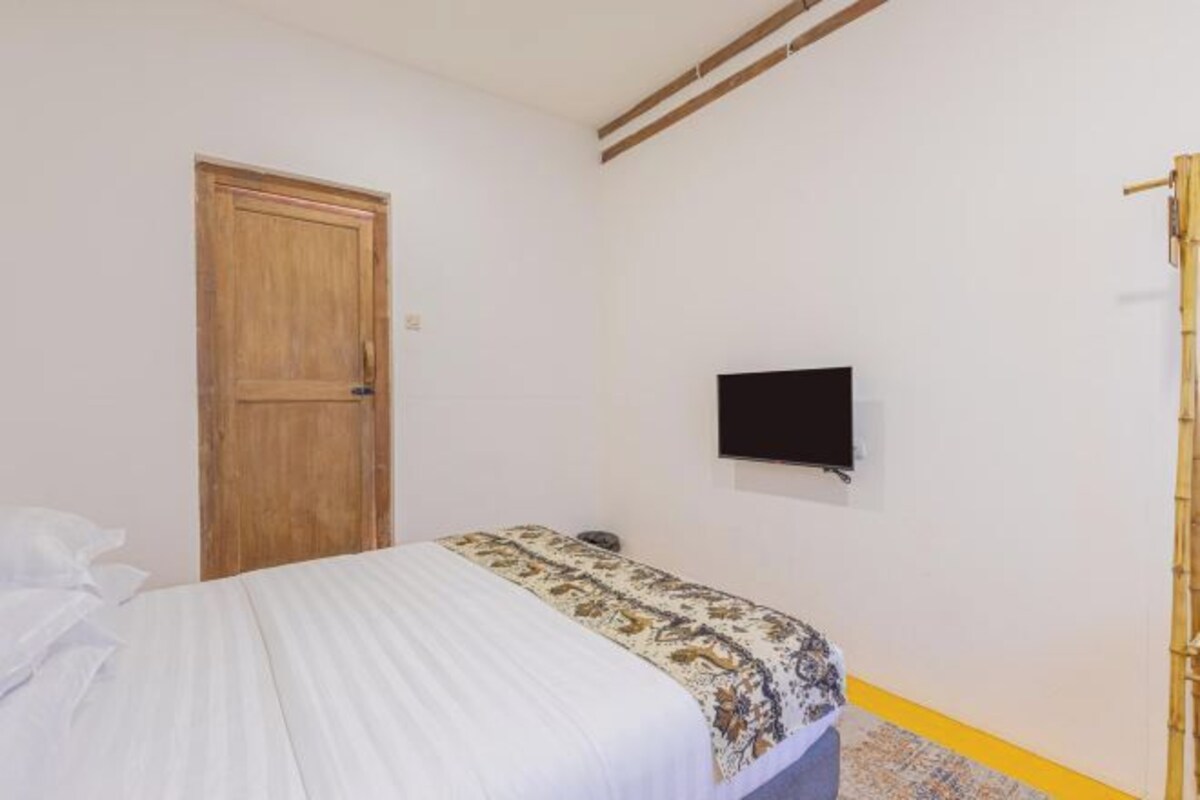 Un dormitorio con cama, una puerta de madera, un televisor montado en la pared y un piso a rayas amarillas.