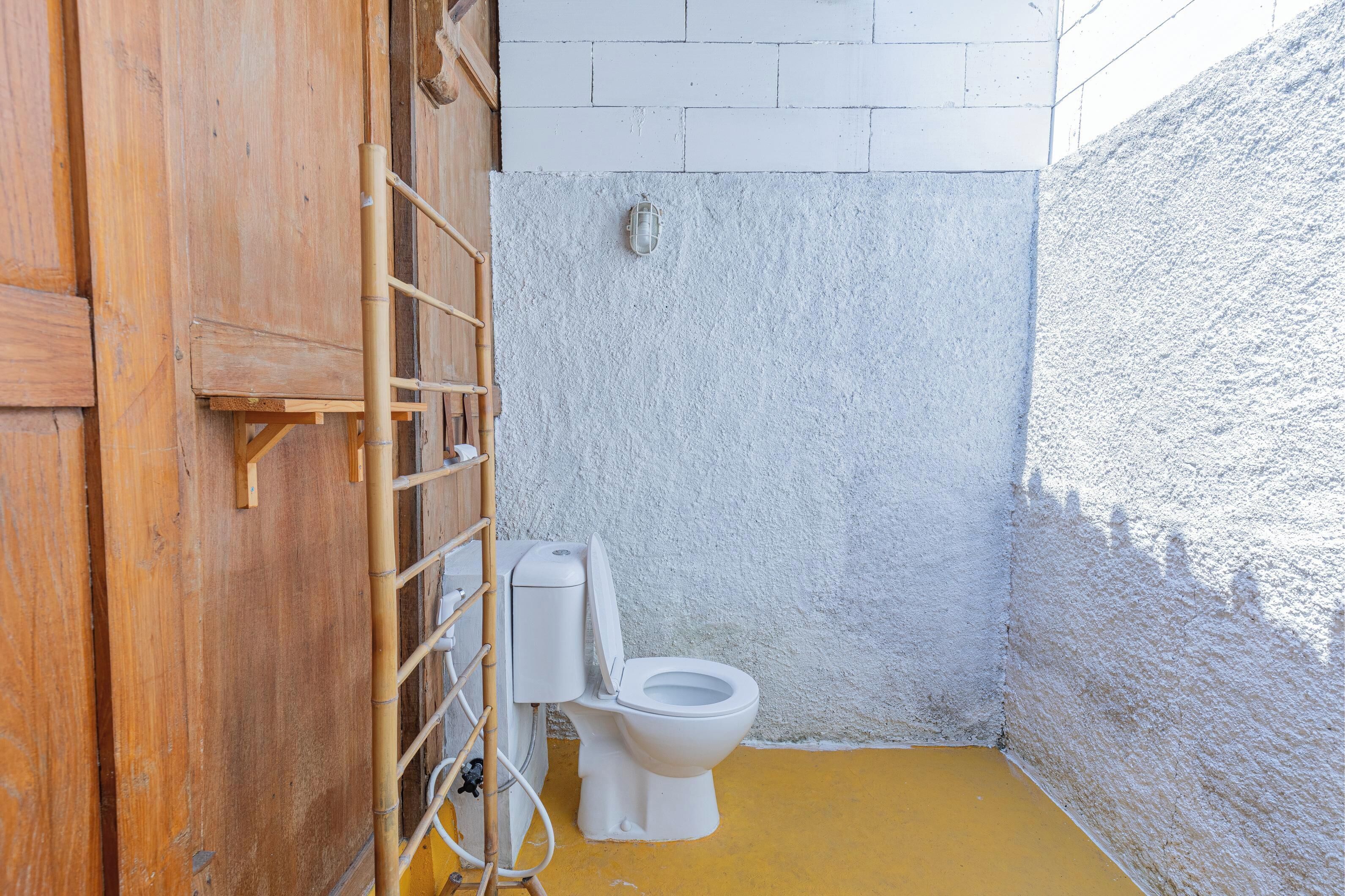 A small, enclosed bathroom with a wooden door, a white toilet, and a yellow floor.
