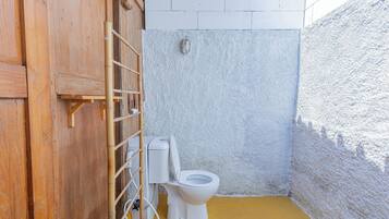 A small, enclosed bathroom with a wooden door, a white toilet, and a yellow floor.