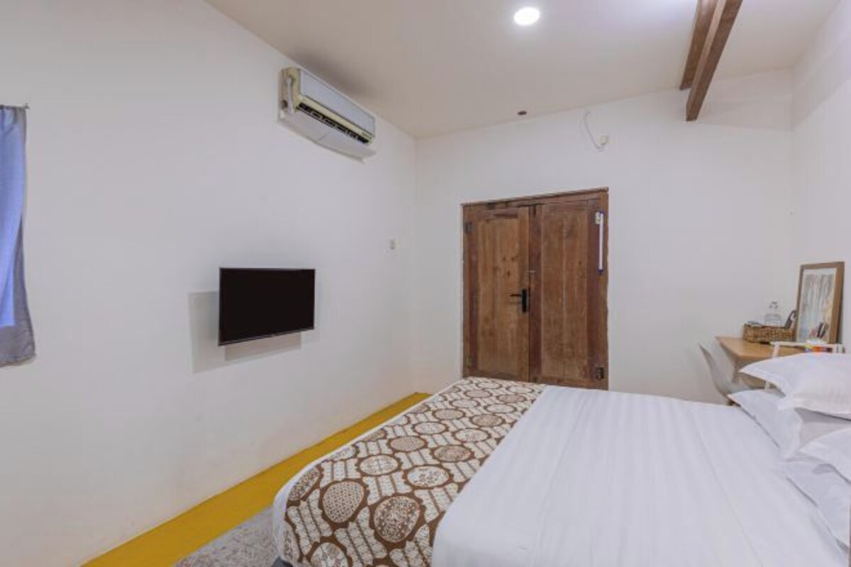 Un dormitorio con cama, televisión, equipo de aire acondicionado y puerta de madera.