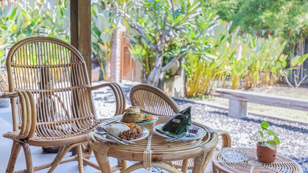 Une table en osier, sur laquelle sont disposés des plats de nourriture et un paquet vert, entourée de chaises en osier et d’une petite plante en pot.