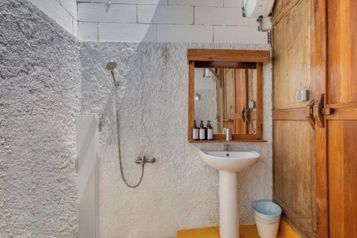 Un baño con lavamanos blanco, armario de madera y zona de ducha.