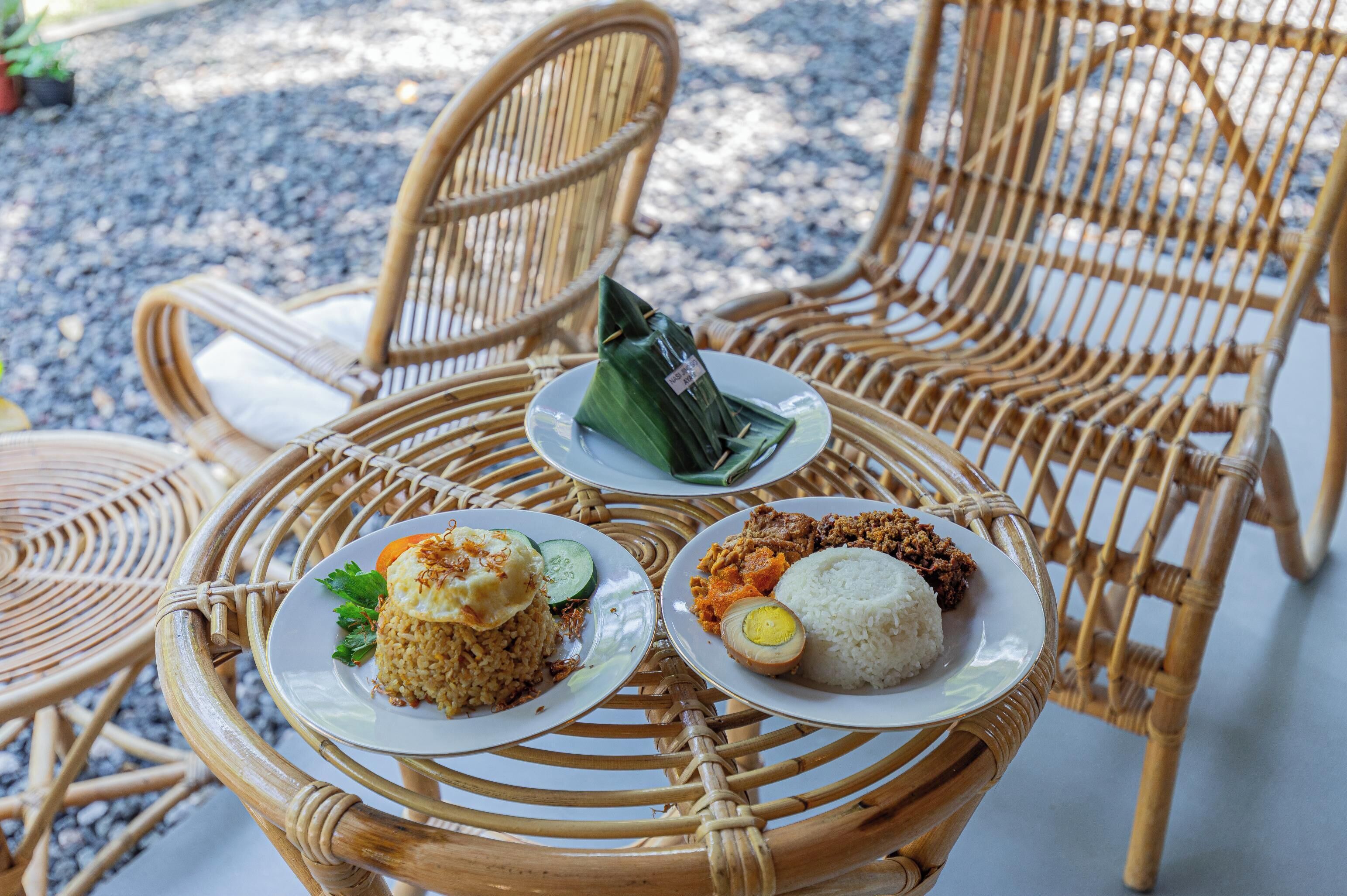 A round wicker table with three plates of food, including rice, vegetables, and a wrapped item.