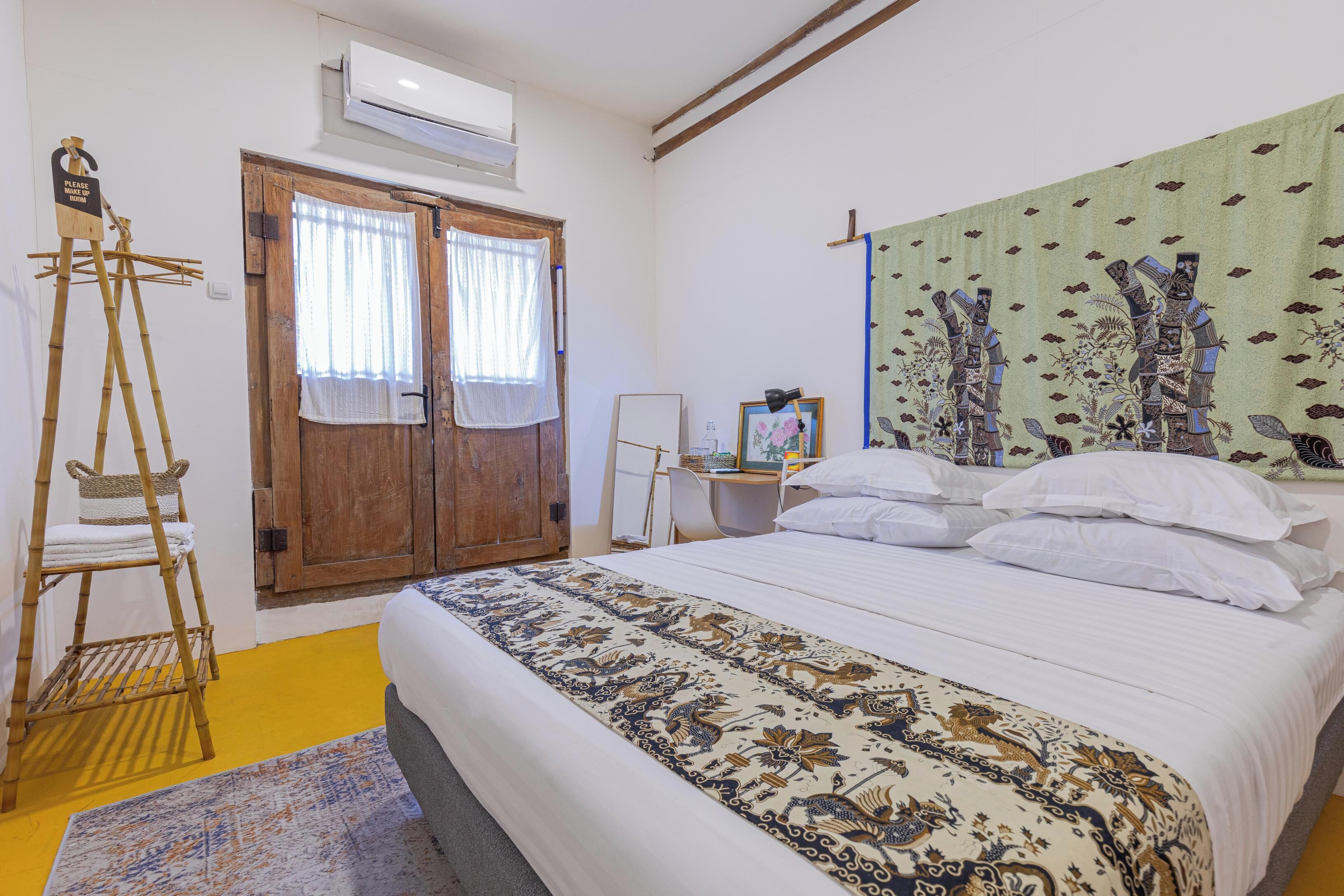 A bedroom with a bed, a wooden wardrobe, a ladder, a desk with a chair, and a wall tapestry.