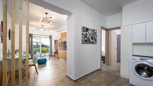 A modern kitchen with a washing machine, wooden flooring, and a dining area with a table and chairs. - Nice n Cosy Apartment in Rhodes Town (Rodos)