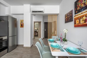Une cuisine moderne dotée d’un réfrigérateur et d’un four en acier inoxydable, un coin repas avec des chaises turquoise et une table blanche, et des œuvres d’art accrochées aux murs.
