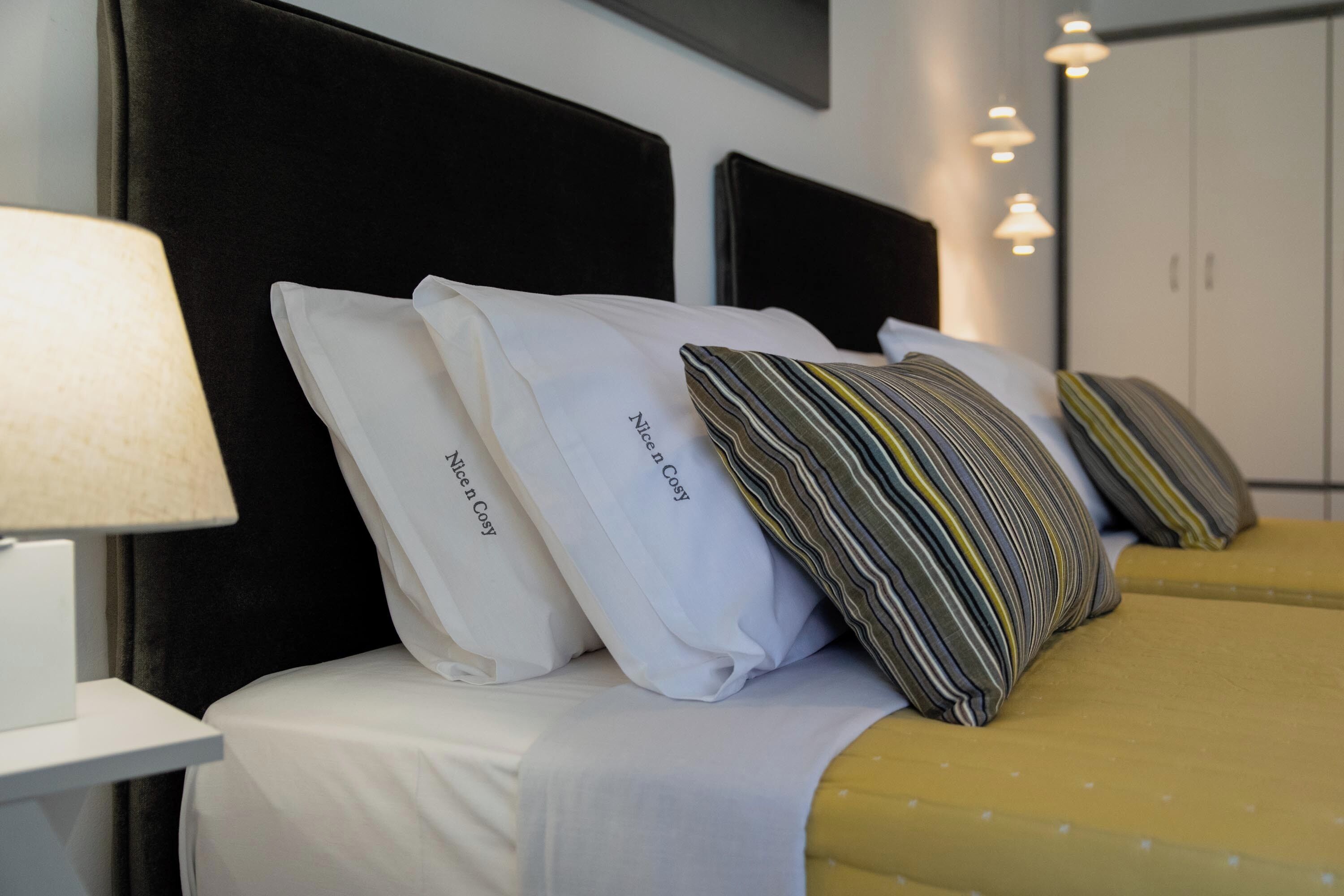 A neatly made bed with white and striped pillows, a yellow bedspread, and a black headboard.