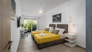 A modern hotel room with two beds, a desk, and a view of greenery. - Nice n Cosy Apartment in Rhodes Town (Rodos)
