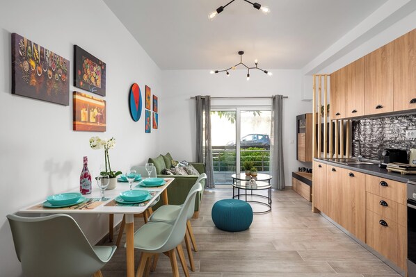 A modern kitchen with wooden cabinets, a dining area with teal chairs, and artwork on the walls.