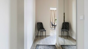 Ein modernes Hotelzimmer mit einem großen Spiegel, einem dunkel gepolsterten Sessel, einem kleinen Tisch mit einer Vase und einem hellen Holzboden.