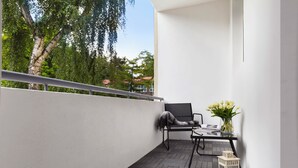 Ein Balkon mit einem schwarzen Stuhl, einem kleinen Tisch und einem Blumenstrauß.