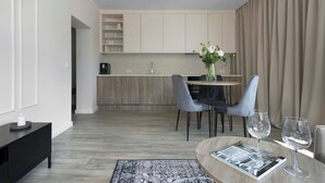 Ein modernes Wohnzimmer mit Essbereich, einer Küche im Hintergrund und einem großen Fenster mit Vorhängen.