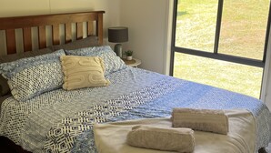 Une chambre avec un grand lit, une table de chevet avec une lampe, une fenêtre donnant sur l’extérieur et un ventilateur de plafond.