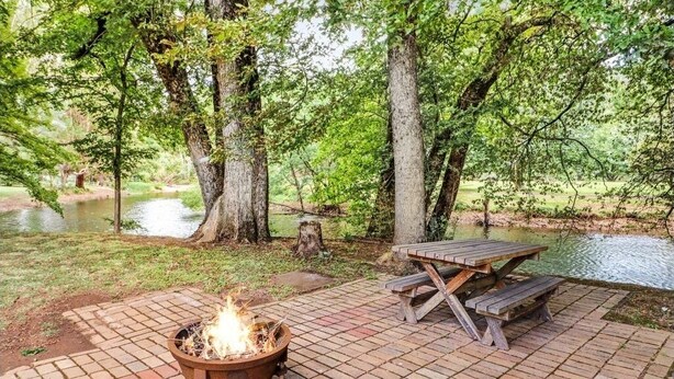 Un espace de pique-nique équipé d’un foyer et de tables de pique-nique, le tout entouré d’arbres et bordé par un plan d’eau.