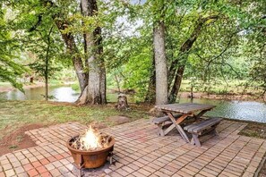 Un espace de pique-nique équipé d’un foyer et de tables de pique-nique, le tout entouré d’arbres et bordé par un plan d’eau.