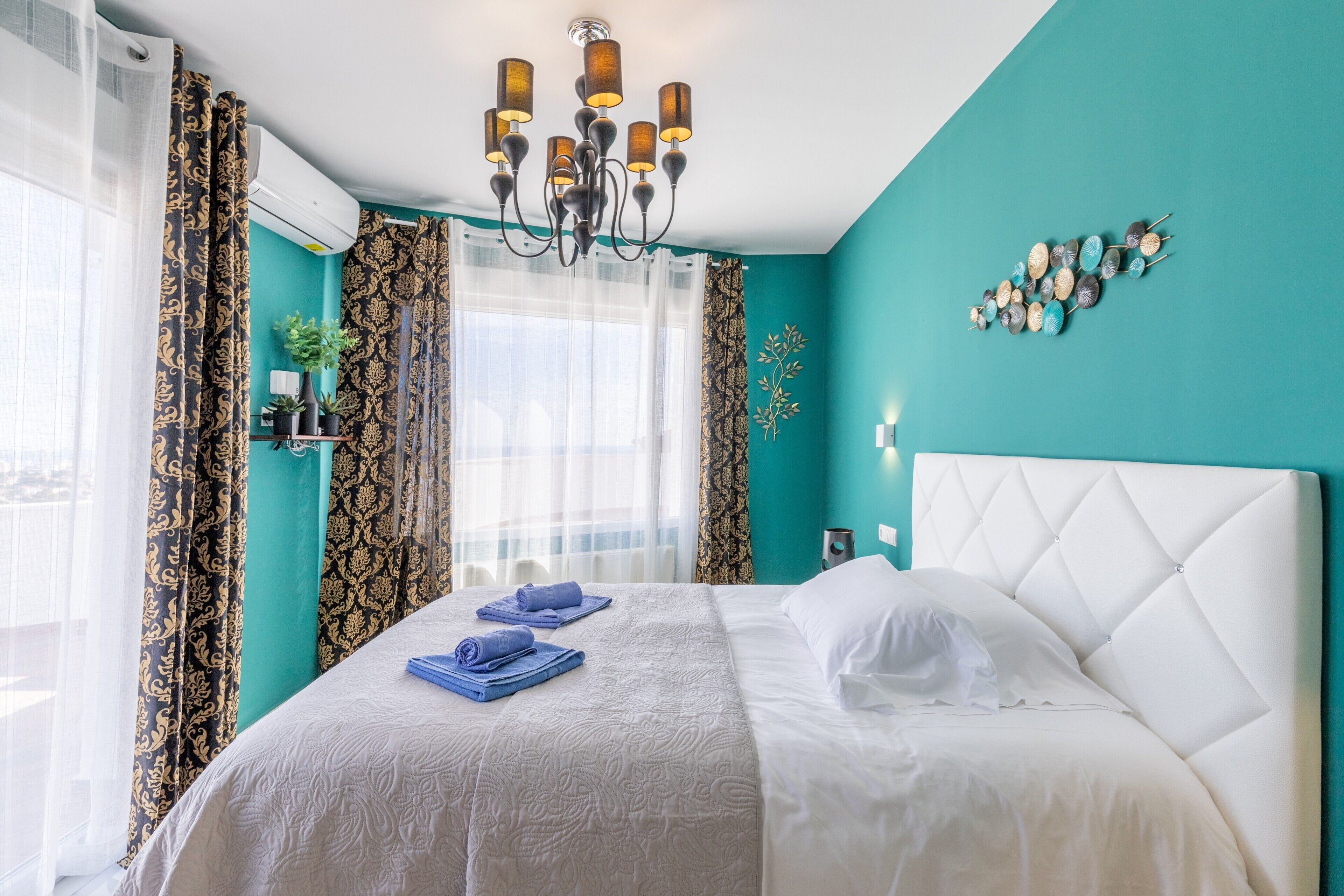 Quarto de hotel com cama, um candelabro, cortinas e um ornamento na parede.