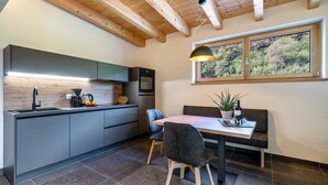 A modern kitchen with a dining area, wooden ceiling beams, and a window with a view of greenery. - Wiesgut Gala Apartment with Mountain View, Balcony, and Wi-Fi (Tesimo)