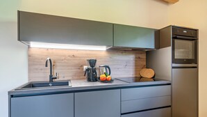 A modern kitchen with a built-in oven, a coffee maker, and a wooden backsplash. - Wiesgut Gala Apartment with Mountain View, Balcony, and Wi-Fi (Tesimo)