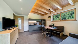 A modern kitchen with a TV, wooden ceiling beams, and a dining area with a table and chairs. - Wiesgut Gala Apartment with Mountain View, Balcony, and Wi-Fi (Tesimo)