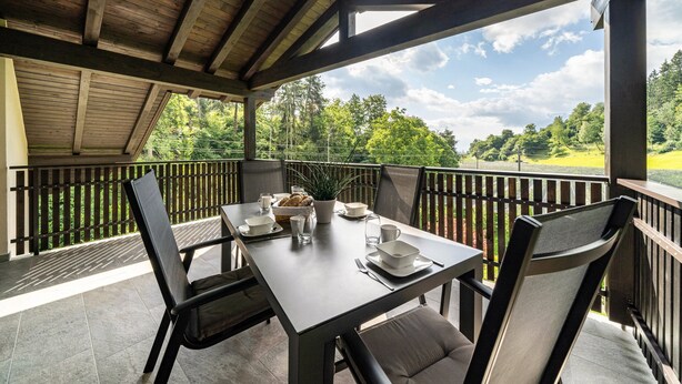 Un'area pranzo all'aperto coperta con un tavolo apparecchiato per due, sedie e vista su un paesaggio verde.