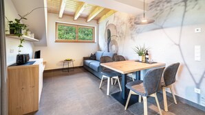 Una cucina moderna con un piano di lavoro in legno, un tavolo da pranzo con sedie, un divano e una finestra vista su del verde.