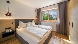A modern bedroom with a large bed, built-in nightstands, a window with curtains, and a hanging light fixture.