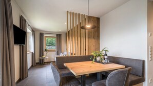A modern dining area with a wooden table, cushioned seating, a TV mounted on the wall, and a wooden slat partition.
