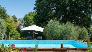 Una piscina con cubierta de madera, rodeada de abundante vegetación y un gran paraguas.
