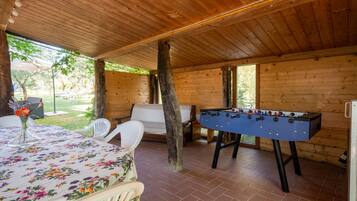 A wooden-floored room with a foosball table, a table with a floral tablecloth, and a white chair.