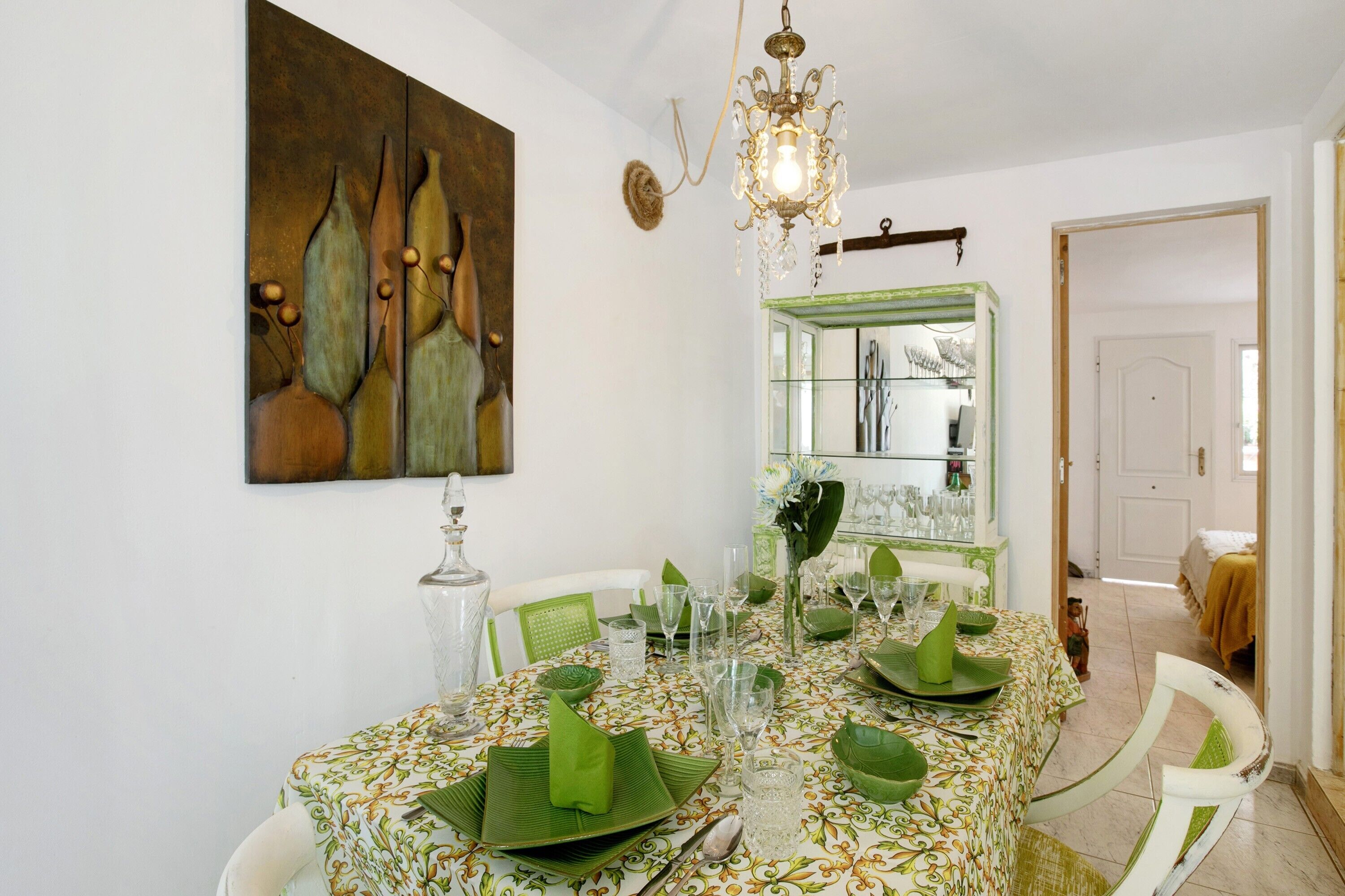 A dining area with a table set for four, a chandelier, and a painting on the wall.