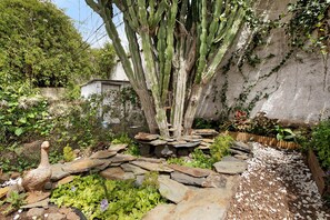 A garden with a large tree, rocks, and a bird statue.
